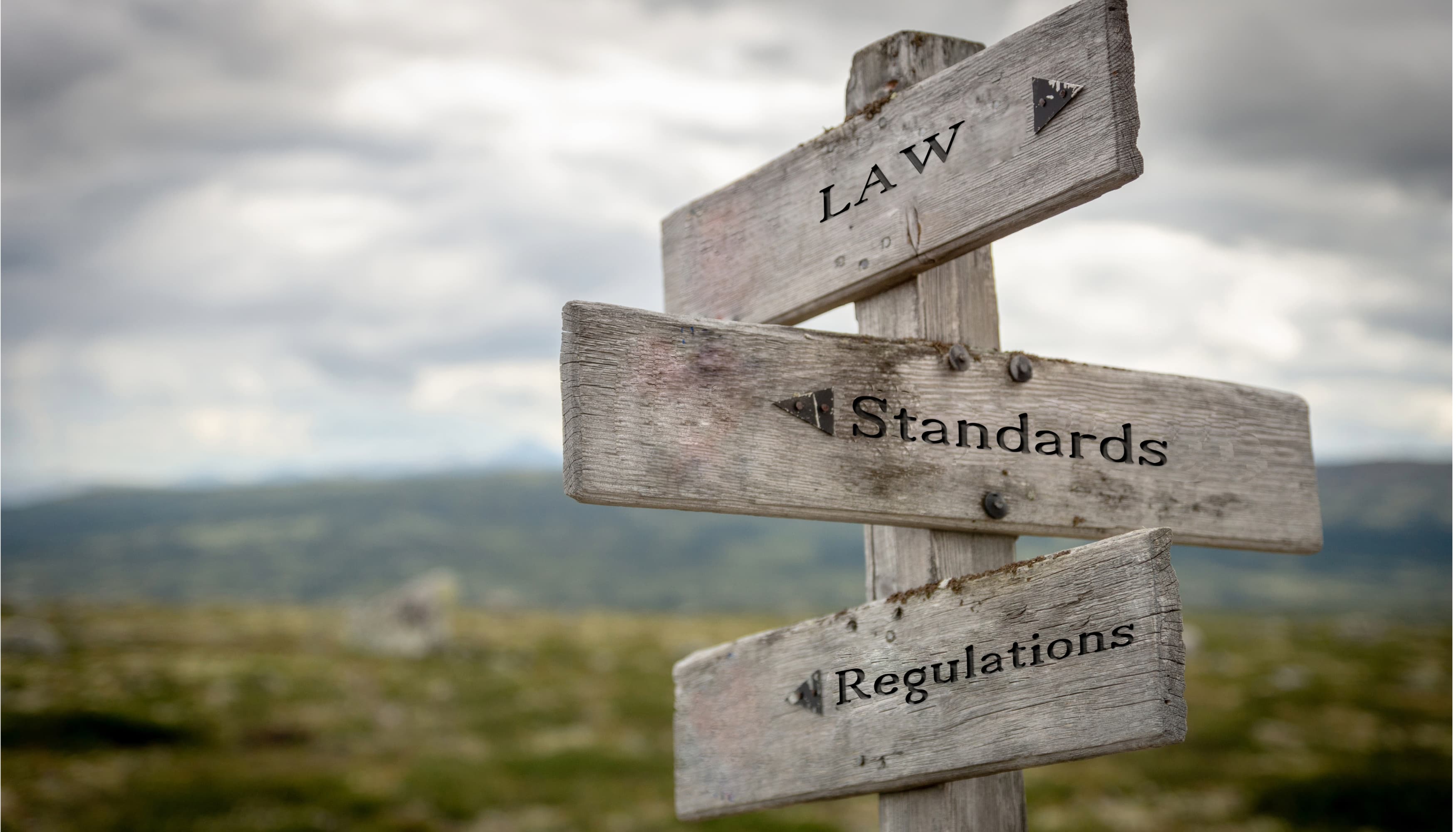 A weathered wooden signpost on open moorland with three arms reading Law, Standards and Regulations.